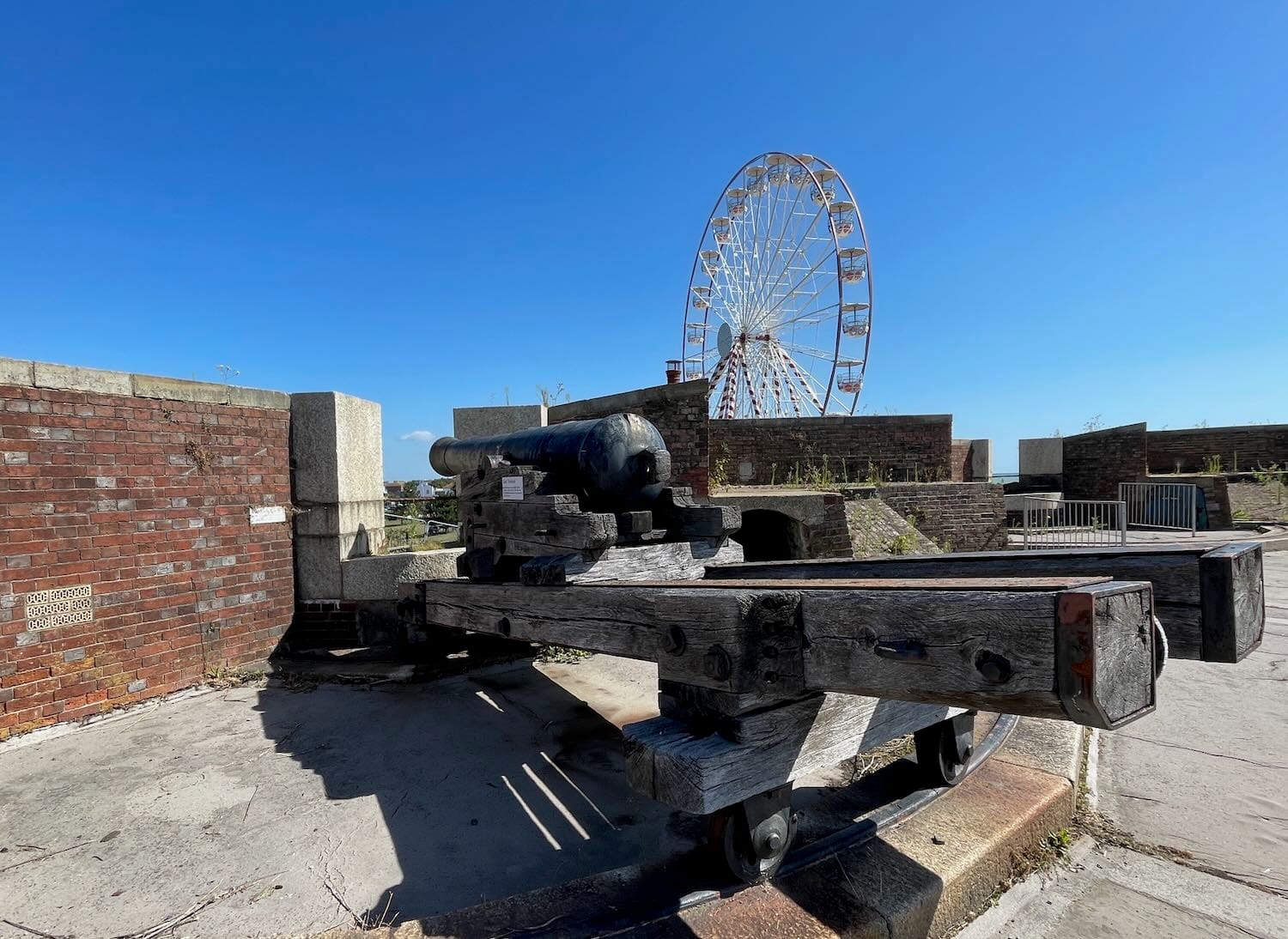 A big wheel against a blue sky seen from the fortress with a historic cannon in the foreground