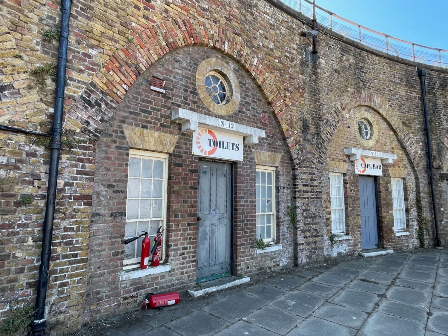 Doors and windows in vaults set in the curving brick wall of a Napoleonic fortress: a toilets and cafe sign are above two of the doors